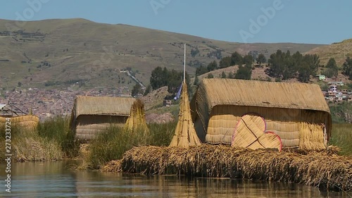 Medium low angle still shot, facing andean ranges, of the back side of  Uros floating reed houses with harvested stacks of totora reeds, Lake Titicaca, Peru