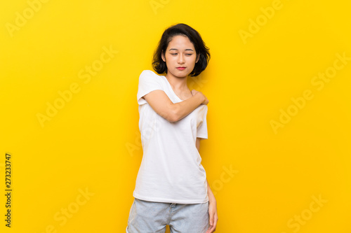 Asian young woman over isolated yellow wall suffering from pain in shoulder for having made an effort