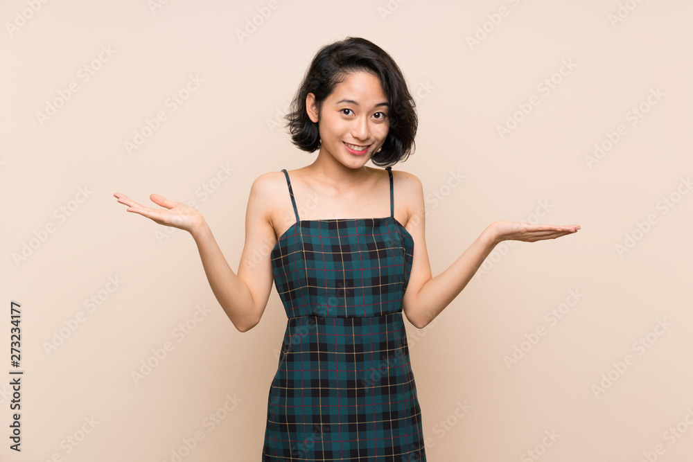 Asian young woman over isolated yellow wall holding copyspace with two hands Asian young woman over isolated yellow wall holding copyspace with two hands