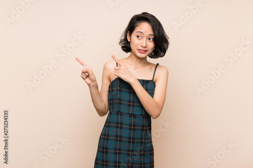 Asian young woman over isolated yellow wall frightened and pointing to the side © luismolinero