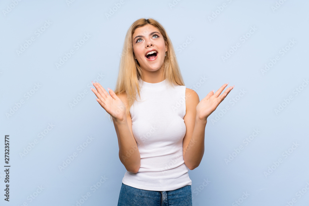 Teenager girl over isolated blue background looking up while smiling