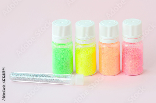 Colorful glitters lies on pastel pink background. Many round jars with multi-colored bright sparkles for nail polish