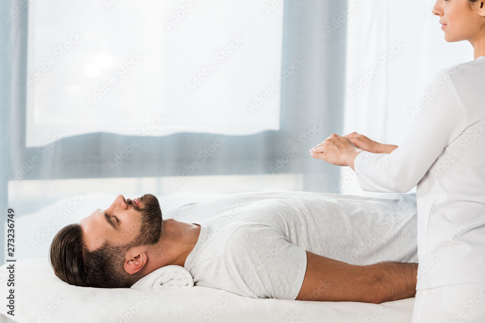 cropped view of healer putting hands above body of bearded man with closed eyes cropped view of healer putting hands above body of bearded man with closed eyes