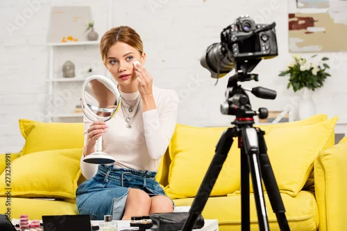Obraz smiling beauty blogger with mirror using decorative cosmetics in front of video camera