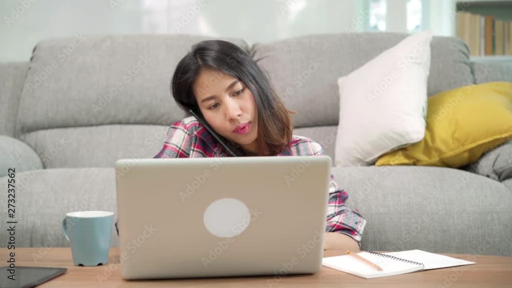 Freelance Asian woman working at home, business female working on laptop and using mobile phone talking with customer on sofa in living room at home. Lifestyle women working at home concept. Freelance Asian woman working at home, business female working on laptop and using mobile phone talking with customer on sofa in living room at home. Lifestyle women working at home concept.