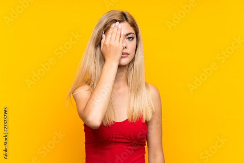 Teenager girl over isolated yellow background covering a eye by hand