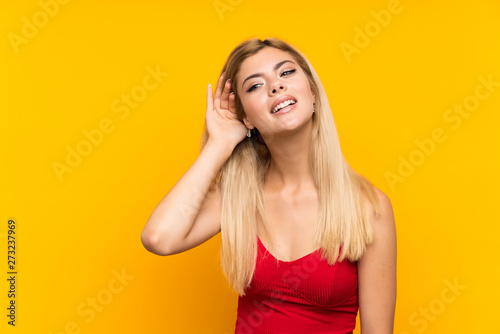 Teenager girl over isolated yellow background listening something