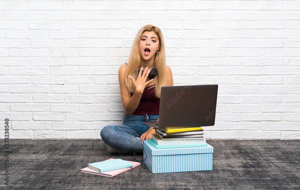 Teenager girl sitting on the floor with her laptop surprised and shocked while looking right Teenager girl sitting on the floor with her laptop surprised and shocked while looking right