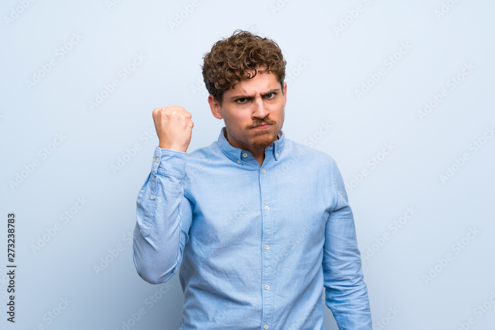 Blonde man over blue wall with angry gesture Blonde man over blue wall with angry gesture