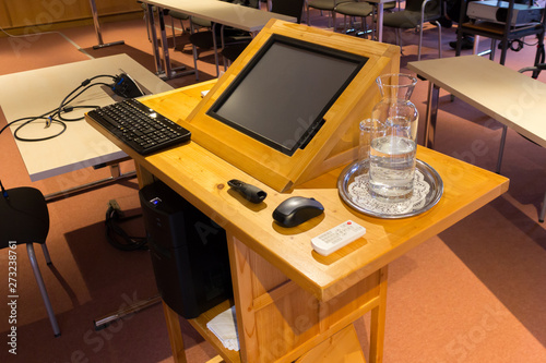 Wooden trubune in a conference or lecture hall with a water pitcher and a computer screen