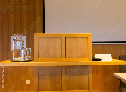 Wooden trubune in a conference or lecture hall with a water pitcher and a projector screen