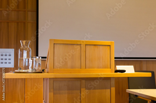 Wooden trubune in a conference or lecture hall with a water pitcher and a projector screen