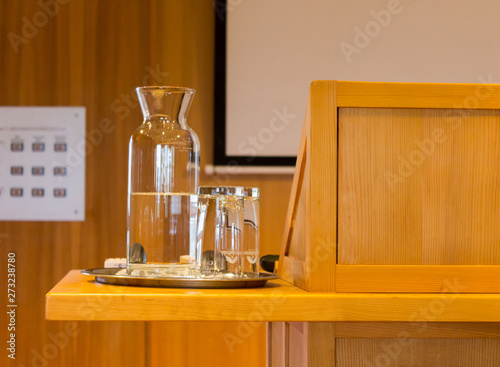 Wooden trubune in a conference or lecture hall with a water pitcher and a white projector screen
