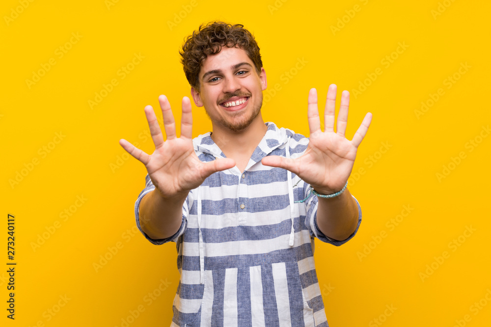 Blonde man over yellow wall counting ten with fingers Blonde man over yellow wall counting ten with fingers