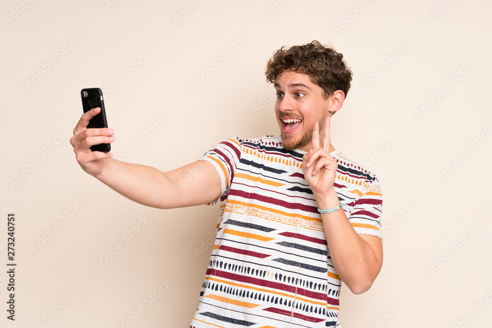 Blonde man over isolated wall making a selfie Blonde man over isolated wall making a selfie