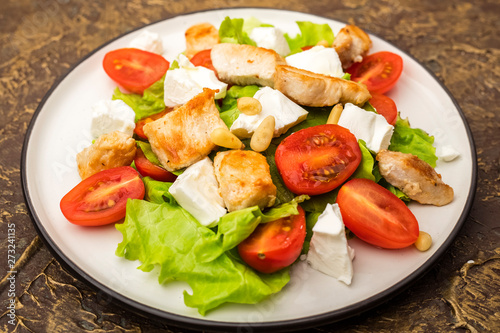 Delicious salad with warm chicken, cherry tomatoes and soft brynza cheese, decorated with pine nuts. dressing with olive oil. dressing with olive oil. Close up