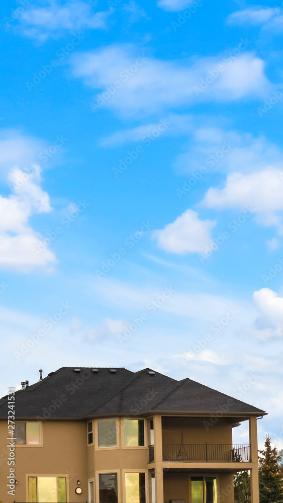 Vertical Three storey home with porch and balcony against blue sky with bright clouds