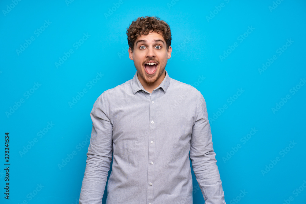Blonde man over blue wall with surprise facial expression Blonde man over blue wall with surprise facial expression