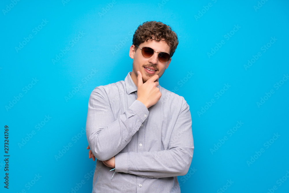Obraz premium Blonde man over blue wall with glasses and smiling