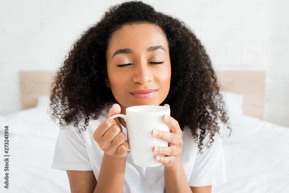 portrait of african american woman closing eyes, holding cup with beverage in hands portrait of african american woman closing eyes, holding cup with beverage in hands