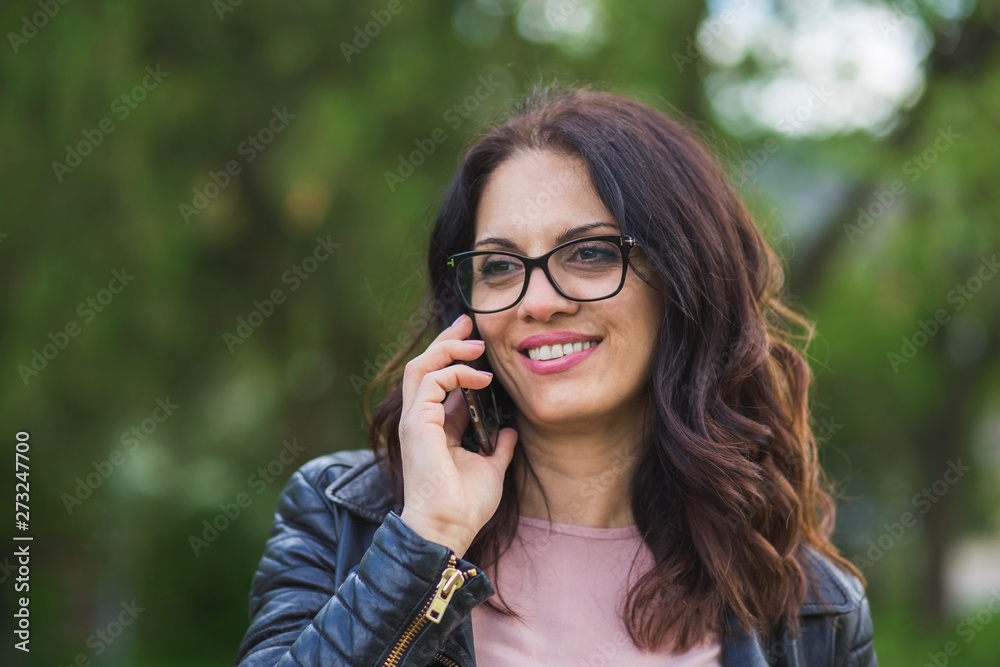 Beautiful middle-age woman in black leather jacket talking on the phone. Springtime, outdoors Beautiful middle-age woman in black leather jacket talking on the phone. Springtime, outdoors