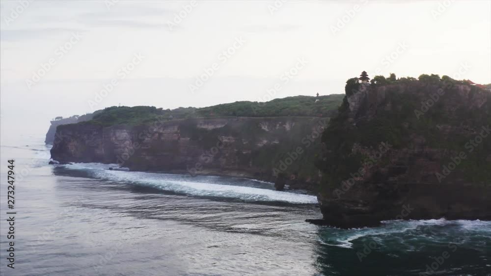Wonderful aerial view of Uluwatu cliff with temple on the top and rocky coastline. Amazing Indian ocean waves breaking at cliffs. Bali, Indonesia Wonderful aerial view of Uluwatu cliff with temple on the top and rocky coastline. Amazing Indian ocean waves breaking at cliffs. Bali, Indonesia