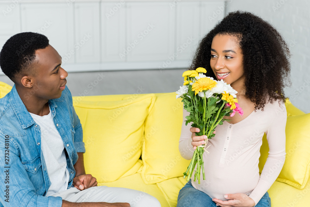 Φωτογραφία pregnant african american holding flowers in hand, and looking at boyfriend