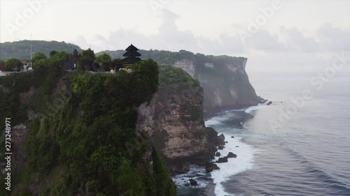 Aerial zooming in veiw of amazing cliff in ocean with Uluwatu Temple, a Balinese Hindu sea temple dedicated to Sang Hyang Widhi Wasa in his manifestation as Rudra. Bali, indonesia photo