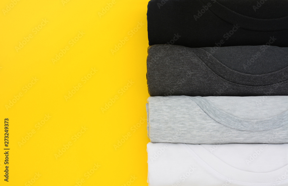 top view stack of black, grey and white (monochrome) t-shirt rolled up on yellow background, copy space, flat lay top view stack of black, grey and white (monochrome) t-shirt rolled up on yellow background, copy space, flat lay