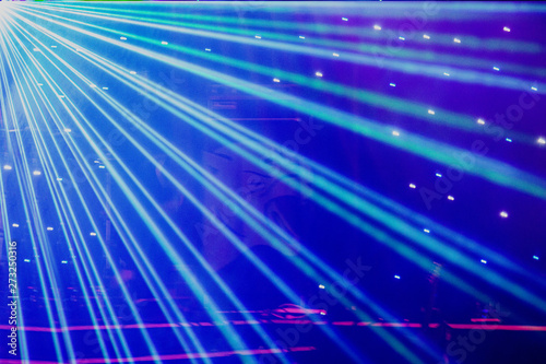 Bright nightclub purple, white, blue laser lights cutting through smoke machine smoke making light and rainbow patterns on the dance floor with bokeh in the background. Mardi Gras