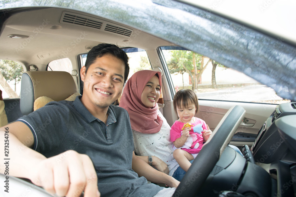 young muslim family , transport, leisure, road trip and people concept - happy man, woman and little girl traveling in a car looking out windows at sunny day