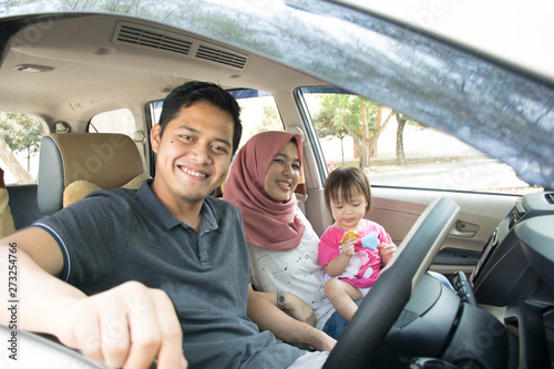 young muslim family , transport, leisure, road trip and people concept - happy man, woman and little girl traveling in a car looking out windows at sunny day