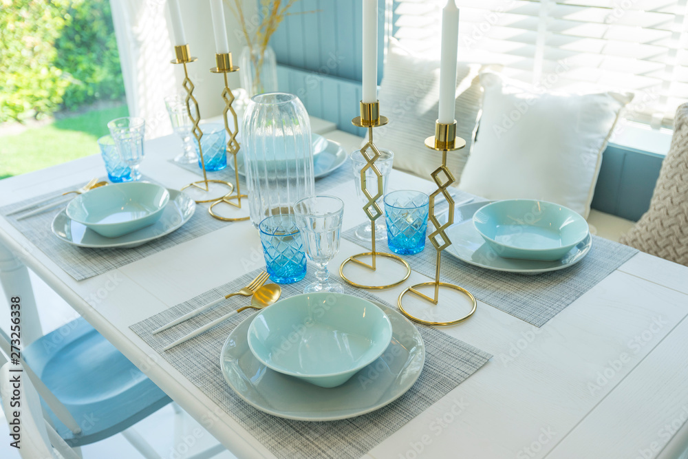 Fototapeta premium Pale blue plate setting on table with gold candle holder in home dining room interior. 