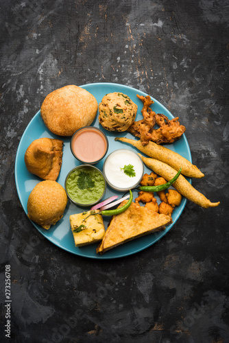 Indian Tea time snacks  in group includes Veg Samosa, Kachori/kachaudi, aloo bonda, khaman dhokla, bread, onion,chilli and moong pakora/pakoda/bhaji/bhajji/Bhajiya/bajji with sauces, selective focus photo