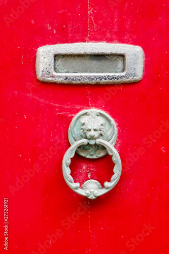 vintage bronze lion head knocker on bright red wooden door with mail slot, Gozo, Malta