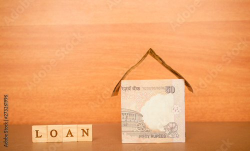 House made from the Indian currency notes and Home Loan in wooden block letters on wooden background photo