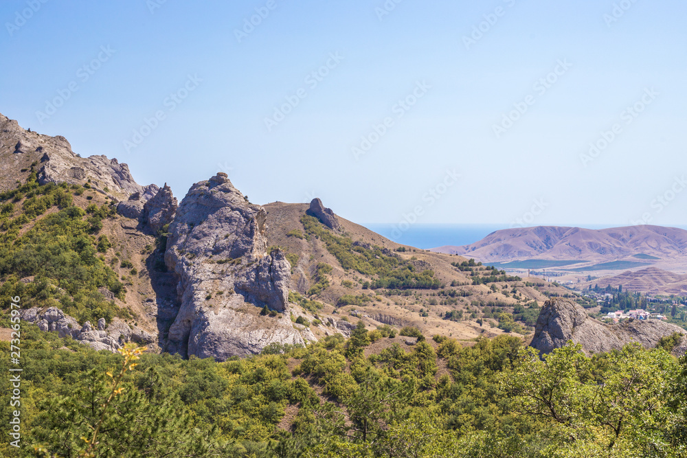 Crimean mountain peaks among green bushes and the sea against the blue sky