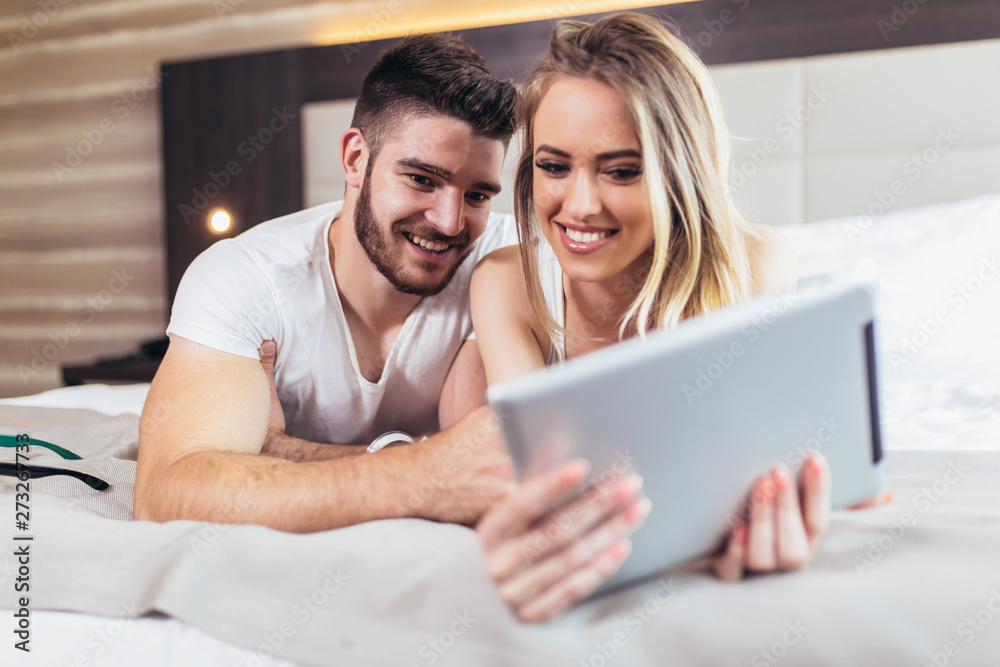 Happy young couple lying on the bed in a bedroom and using digital tablet. Happy young couple lying on the bed in a bedroom and using digital tablet.