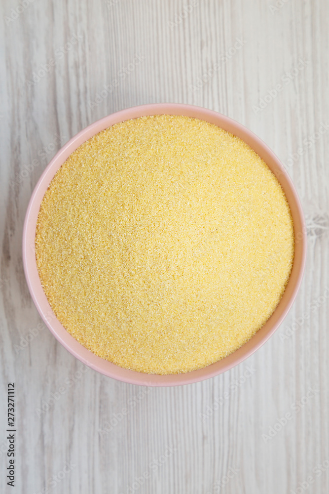 Dry semolina durum flour in a pink bowl over white wooden background, overhead view. Top view, from above, flat lay.
