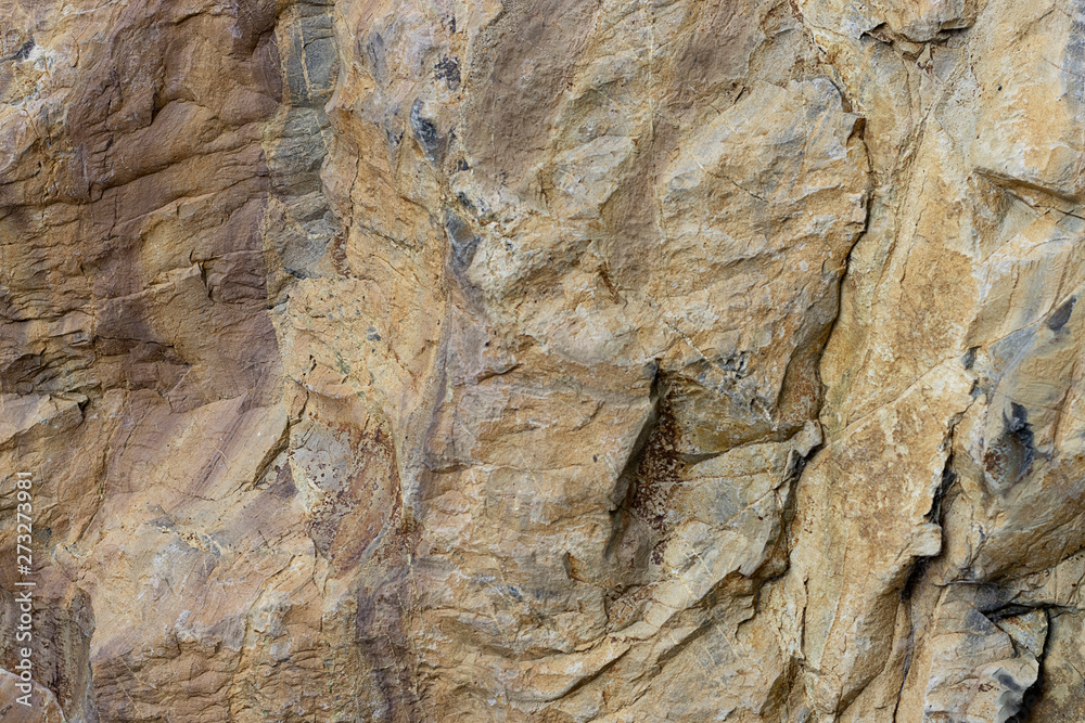 Natural stone relief brown color. Background rock with a texture of yellow with small cracks. Weathered stone layers of different colors.