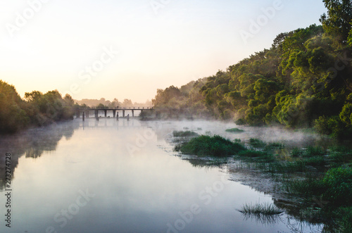 The guy with the bike on the bridge. Mist rises above a river surrounded by trees