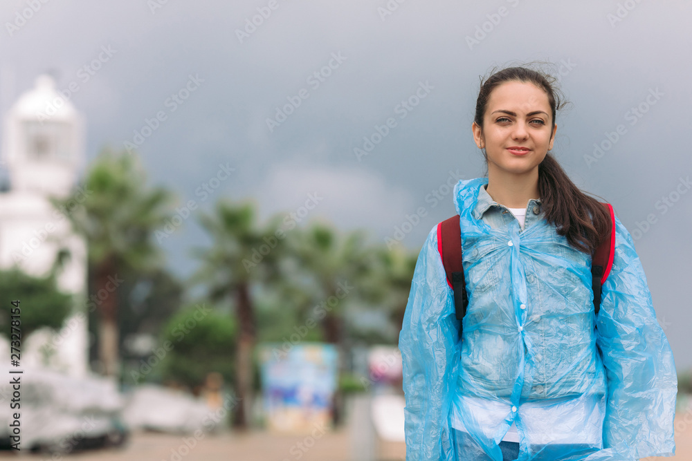 young woman tourist in raincoat with backpack smiling and looking at the camera