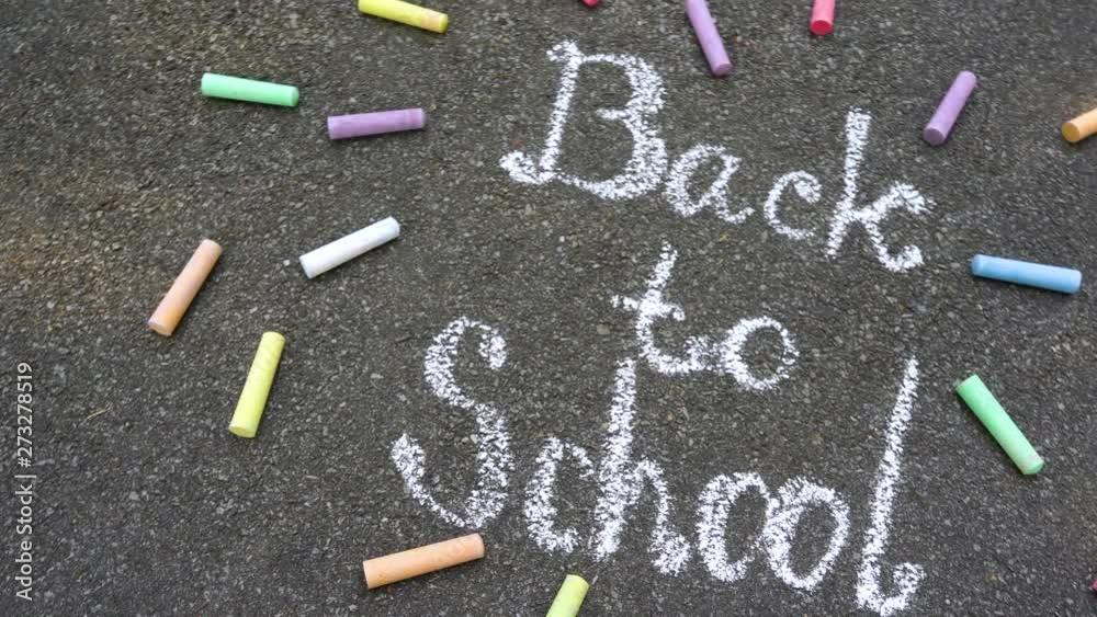 Closeup top view of phrase Back to school drawn with white chalk on grey surface of sidewalk. Real time 4k video footage.