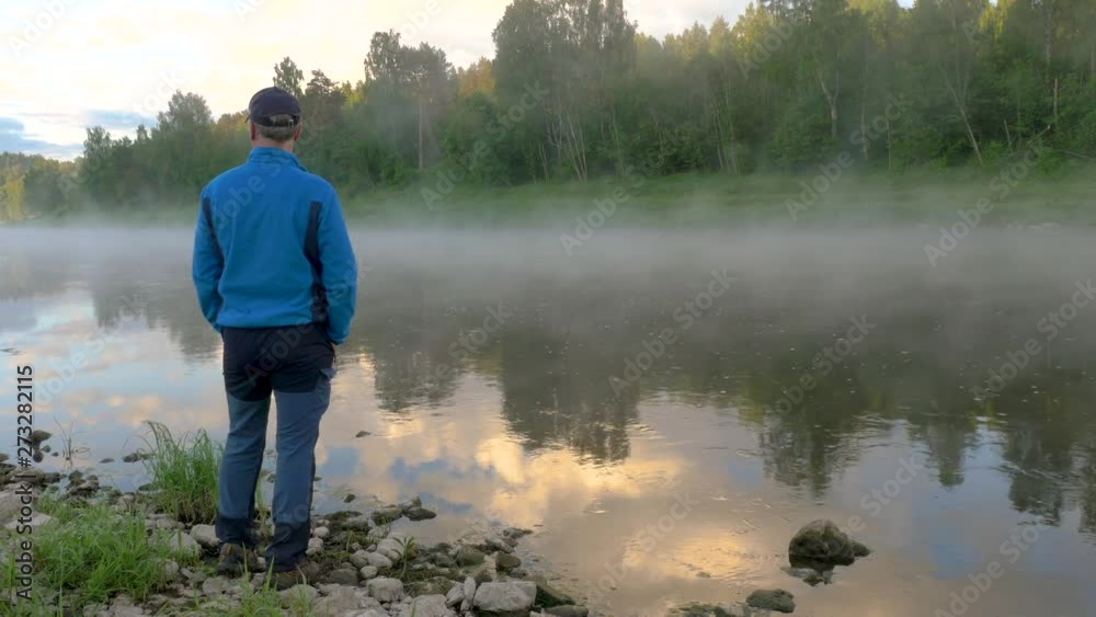 man enjoys clear lake with morning fog and reflecting sky man enjoys clear lake with morning fog and reflecting sky