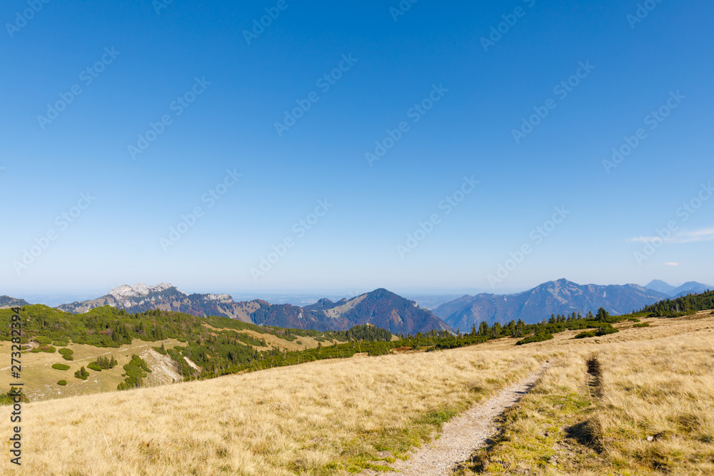 Rolling Hills on Mountain Range near Mountain Geigelstein, Schleching, with dry grass, Mountains Kampenwand, Hochplatte, Hochfelln and Hochgern in background
