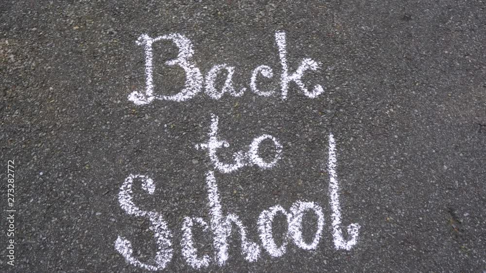 Closeup top view of phrase Back to school drawn with white chalk on grey surface of sidewalk. real time 4k video footage.