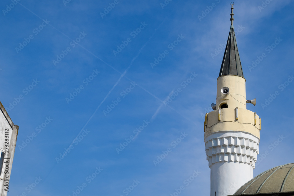 tower of the minaret of the mosque against the blue sky and the contrail from aircraft.