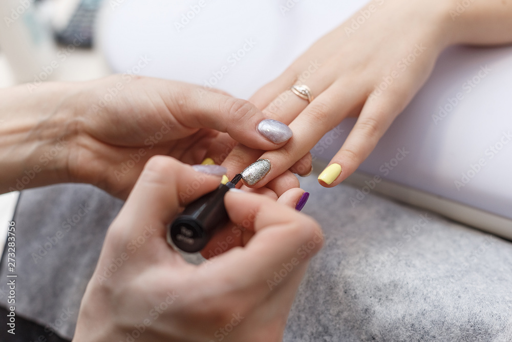 Closeup of beautiful hands applying transparent nail polish in beauty salon. Manicurist hand painting client's nails