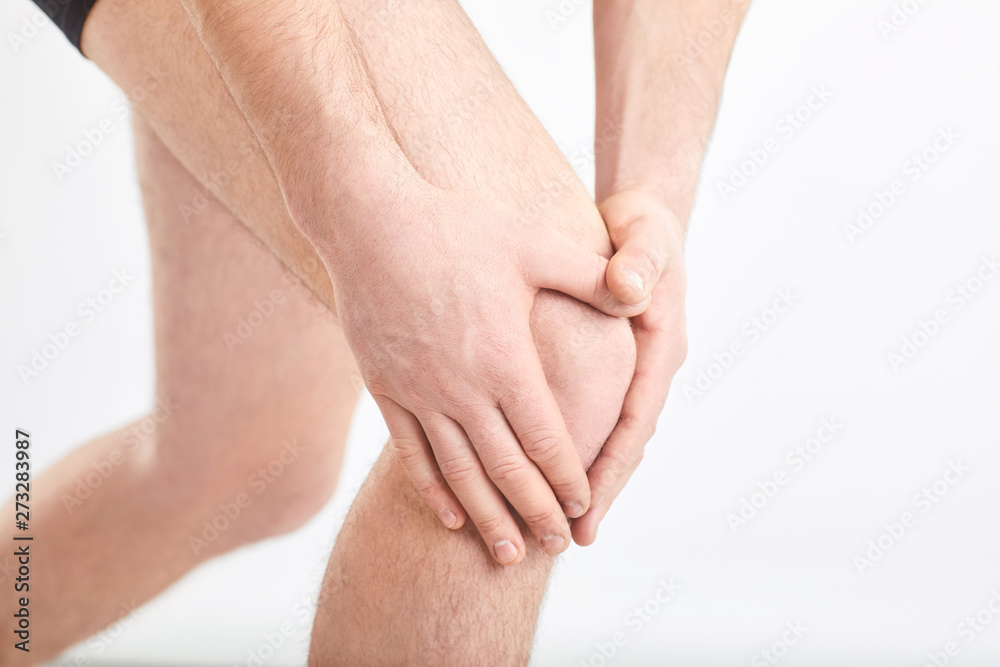 A man in underwear holds his knee with a hand on a gray background. A man in underwear holds his knee with a hand on a gray background.