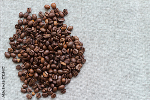 Roasted coffee beans on a grey textile background, top view, left side, free space